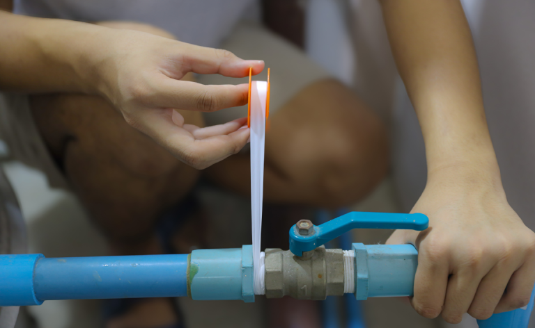 A person uses plumbers’ tape on a PVC pipe