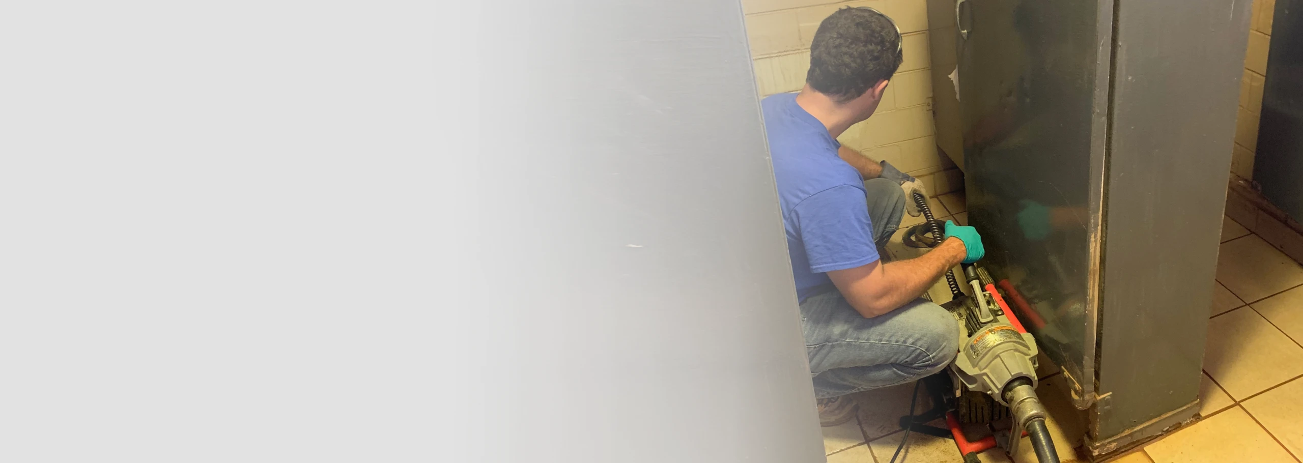 PlumbWize plumber performing commercial drain cleaning in a shower stall