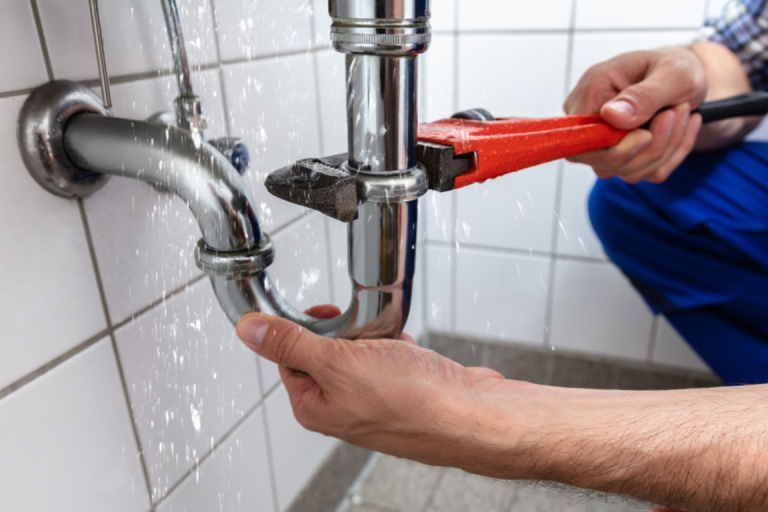 Plumber fixing a leaking pipe with a red wrench.