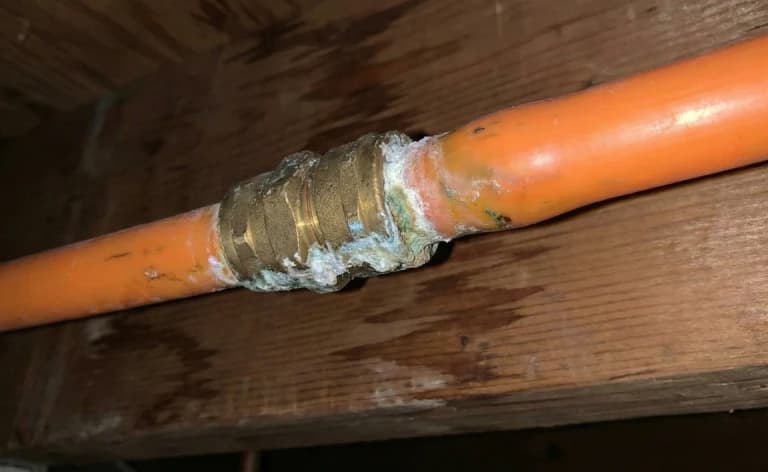 White and green buildup around a coupling on an orange pipe.