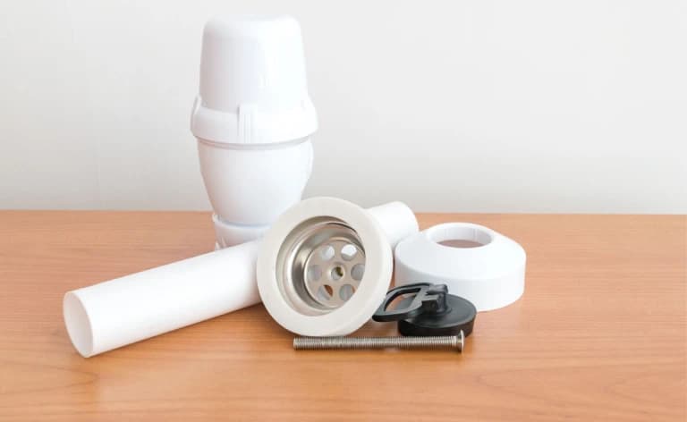 A sink drain strainer and white plastic fittings on a worktop.