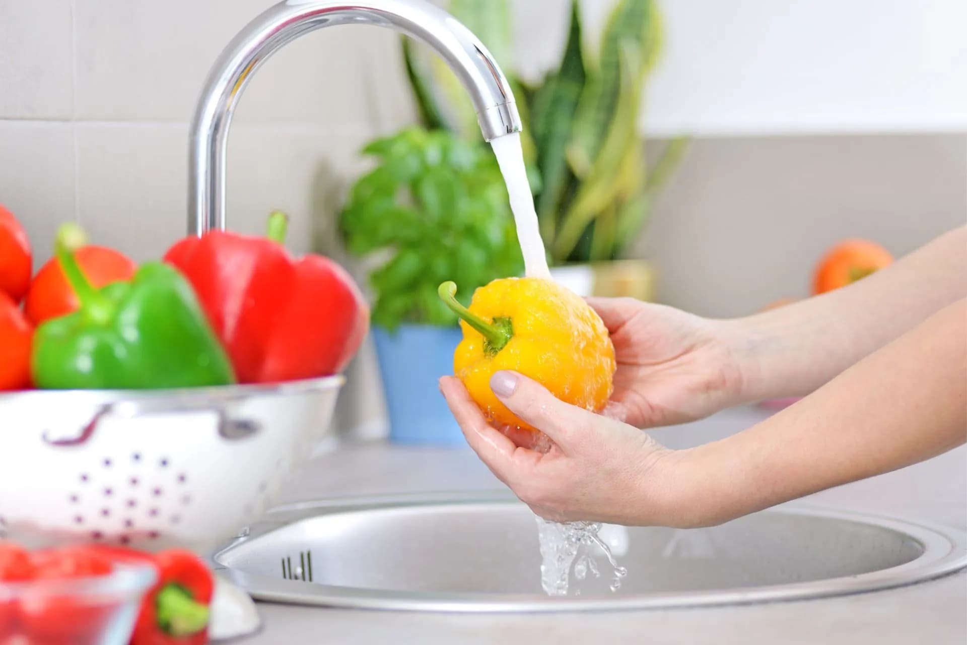 A person washing a yellow bell pepper in a kitchen sink