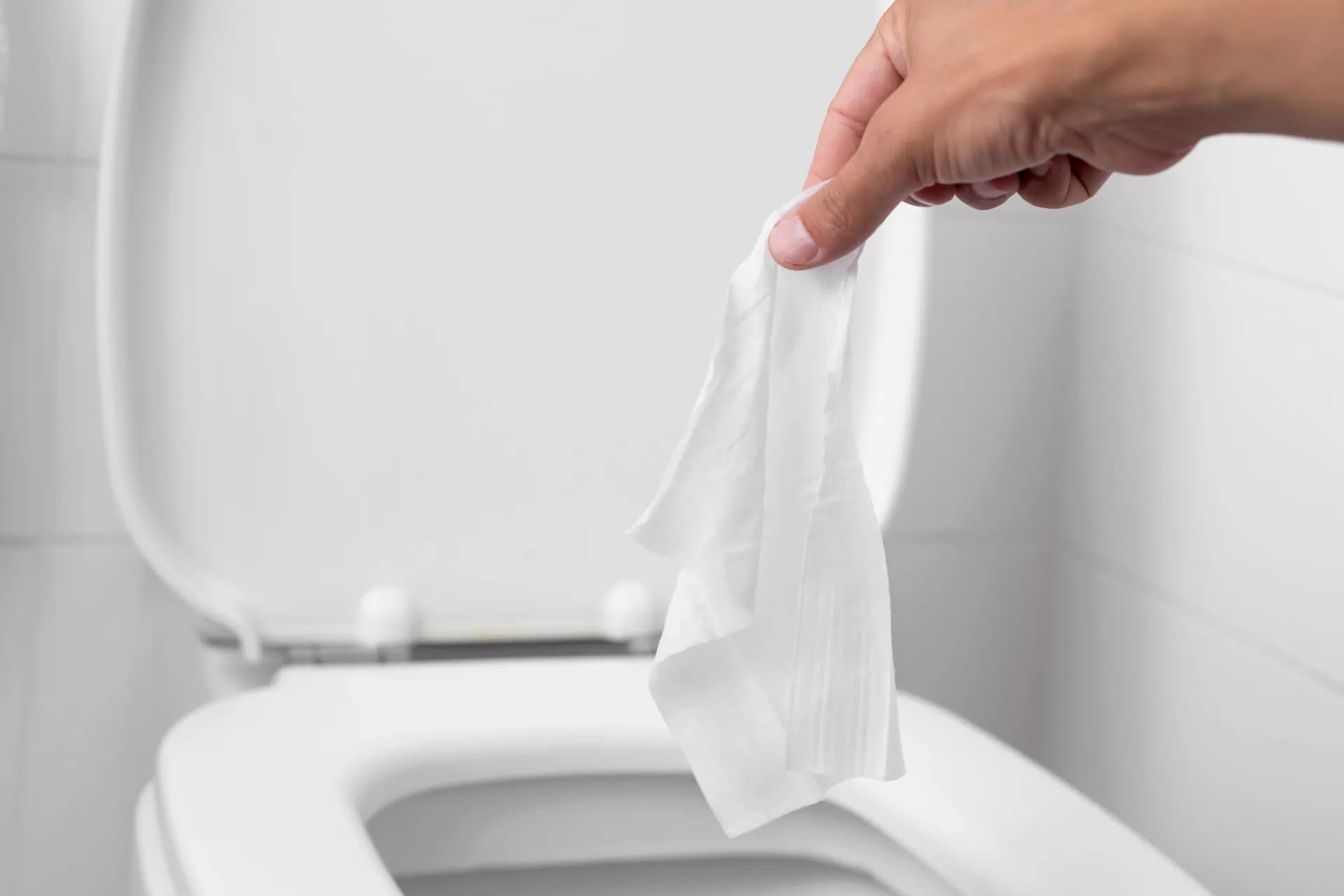 A person throwing a wet wipe into a toilet bowl