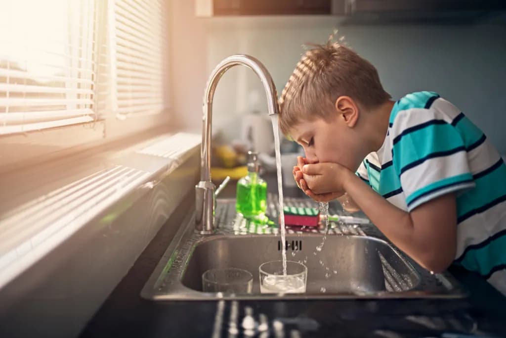 a young child drinks water directly from the tap