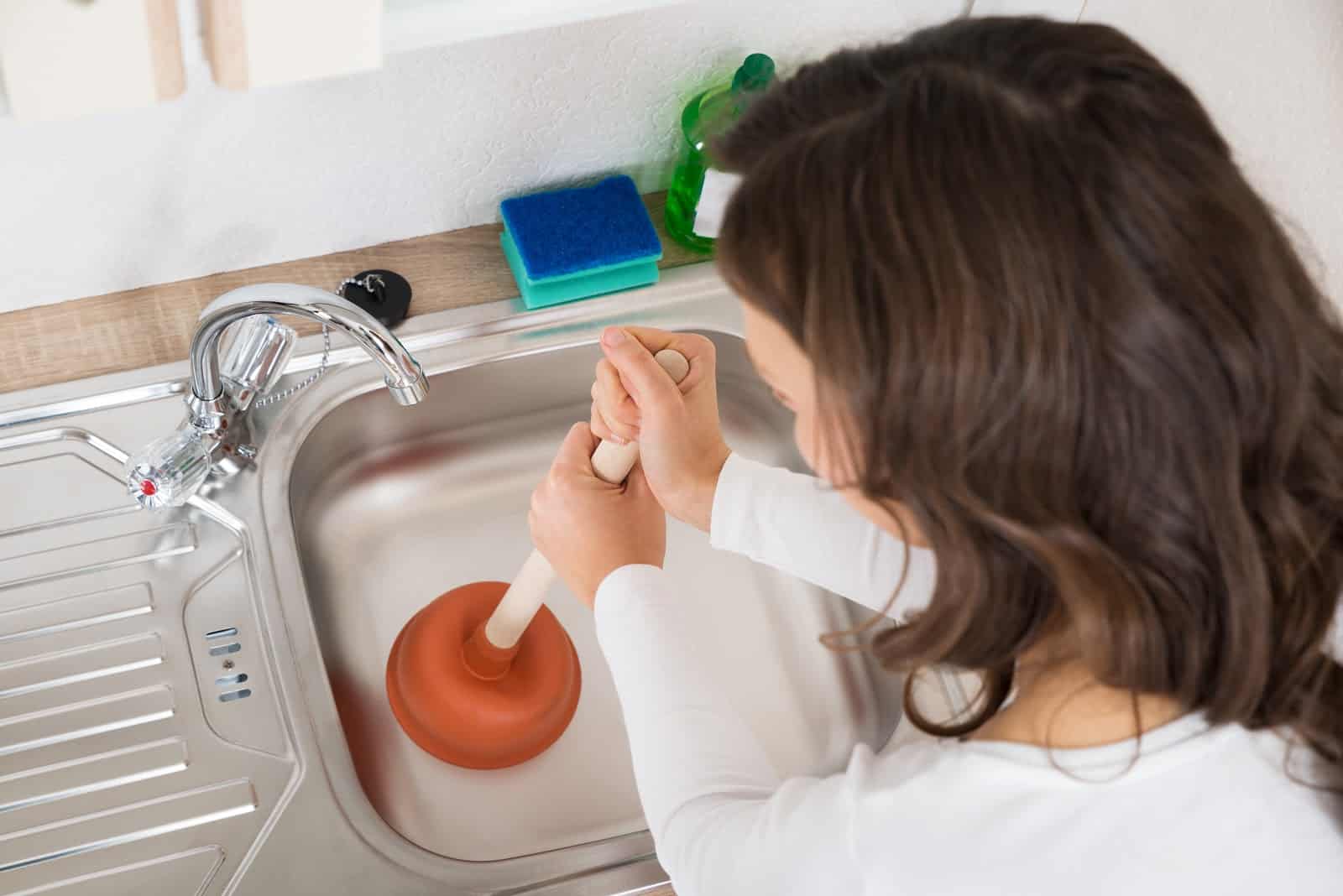 Close up of a woman using a plunger to clean a kitchen sink drain