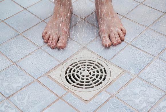 Close up of feet standing next to a shower drain
