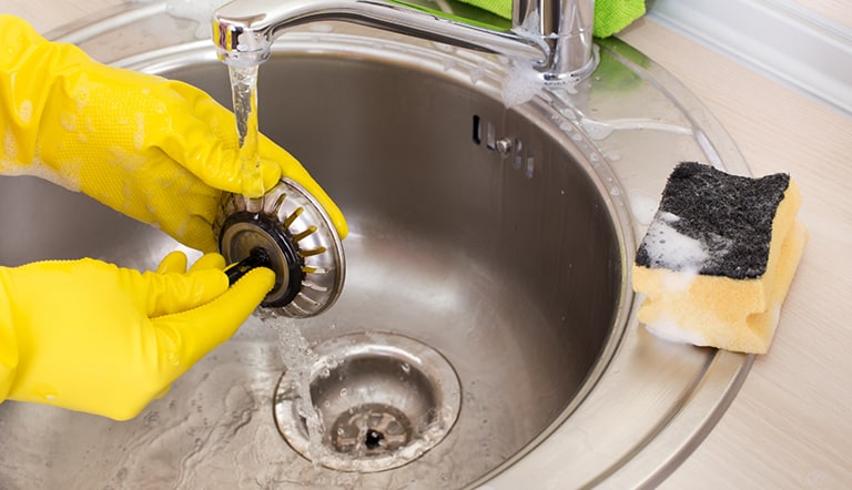 An individual cleans their kitchen sink drain