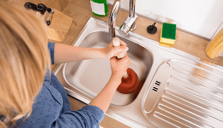 Top view of a woman using a plunger to unclog a sink