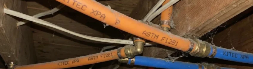 Exposed ceiling with orange and blue Kitec pipes labelled “Kitec XPA,” connected with metal fittings and running through wooden joists