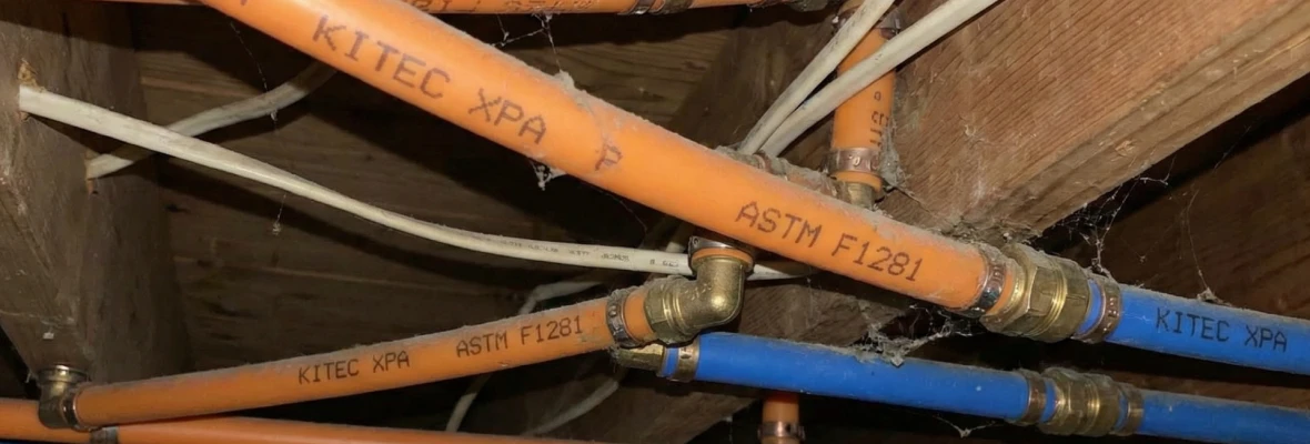 Exposed ceiling with orange and blue Kitec pipes labelled “Kitec XPA,” connected with metal fittings and running through wooden joists