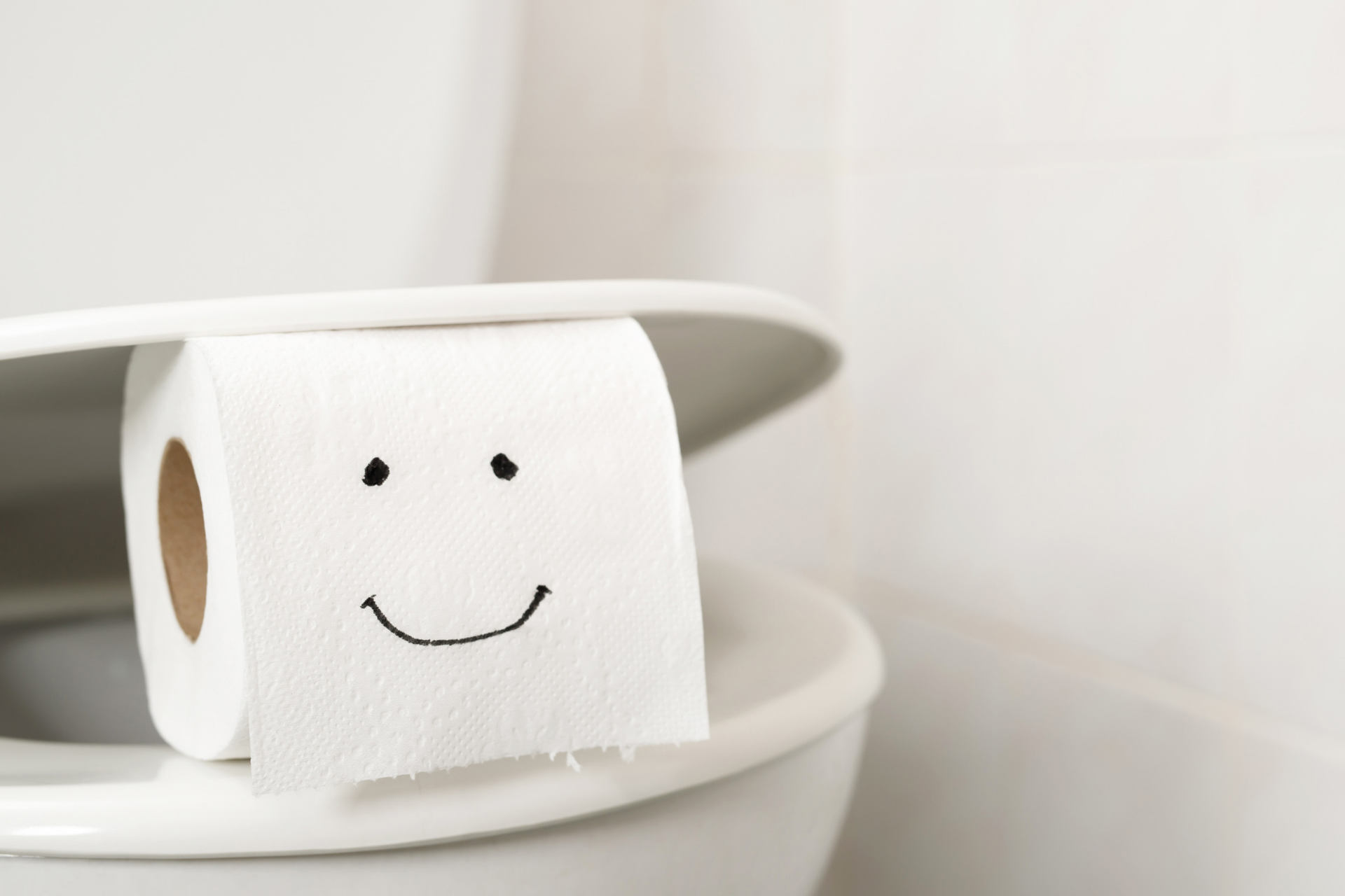 A smiley face drawn onto a roll of toilet paper atop a toilet seat