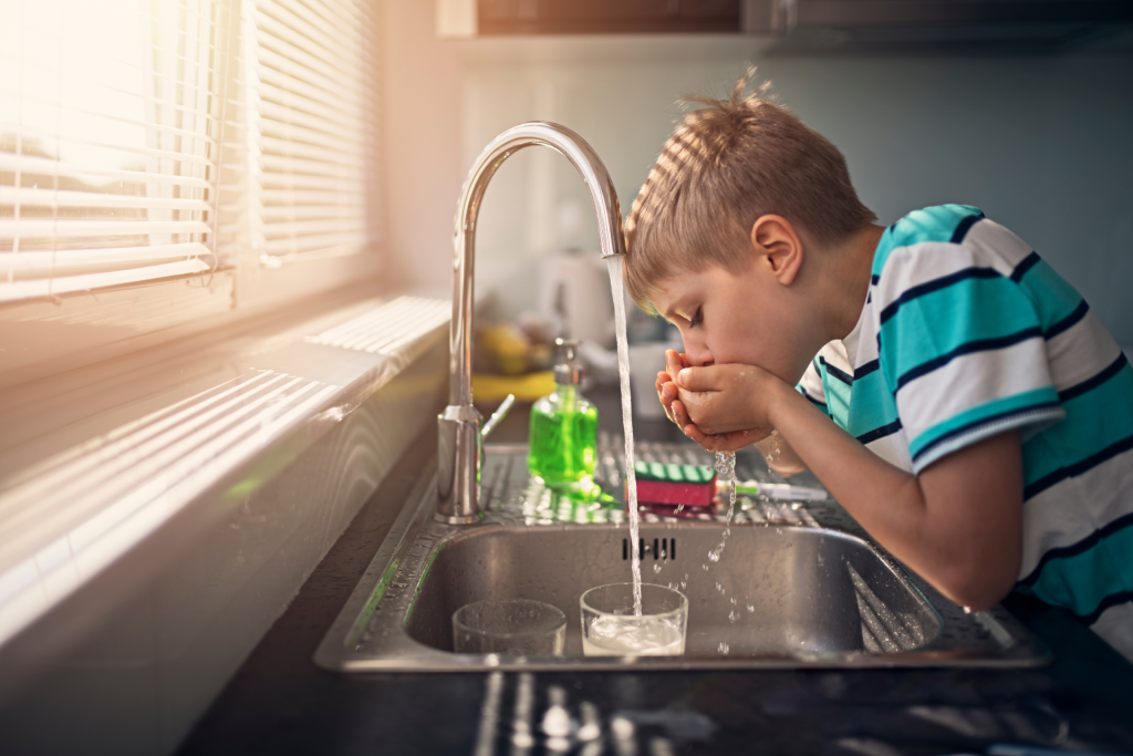 a young child drinks water directly from the tap