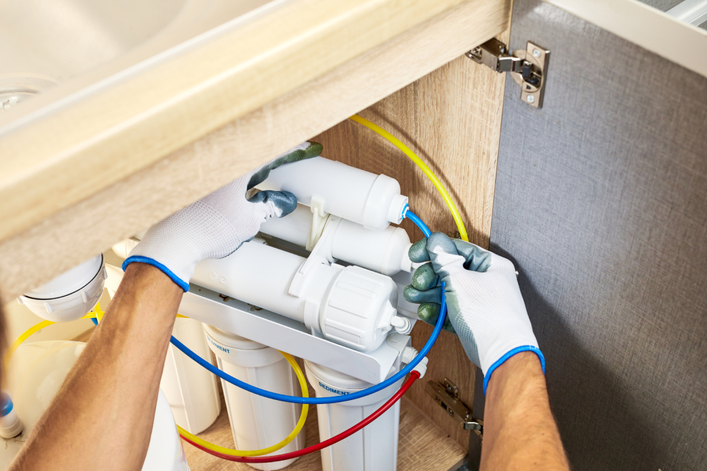 A plumber installing a water filtration system under a sink 