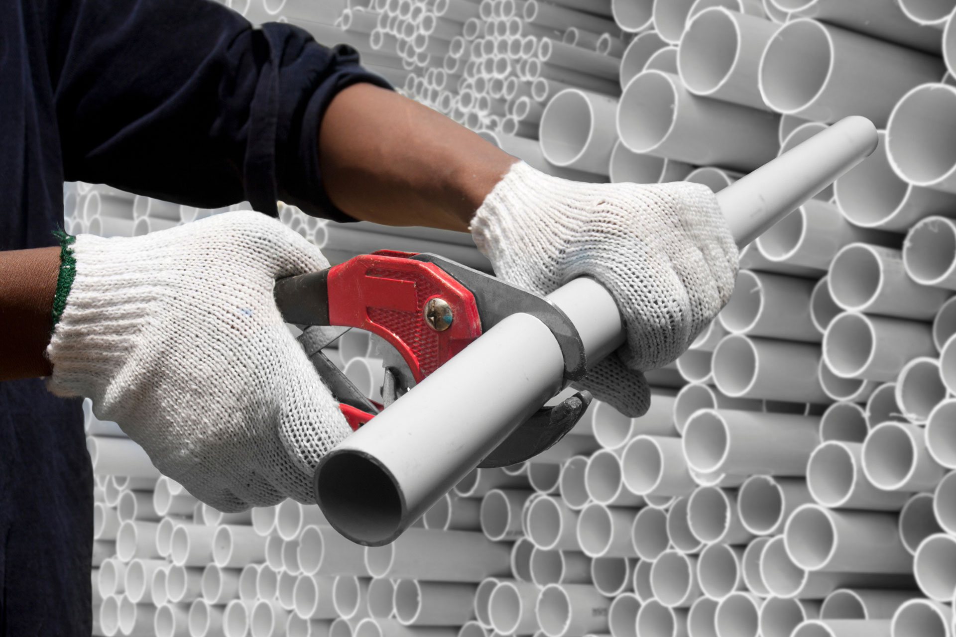 A plumber cutting a PVC pipe to shorten its length 