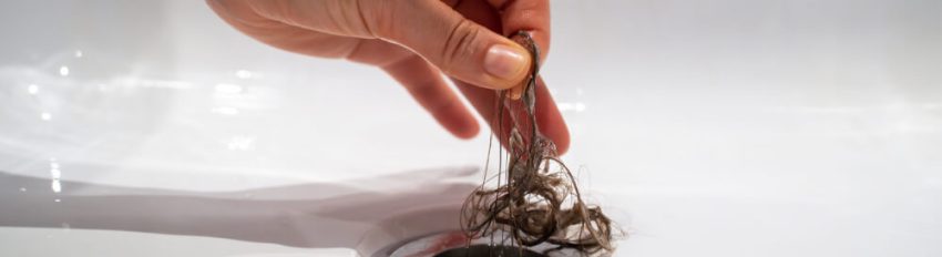 A person removing a substantial amount of wet hair from a tub drain