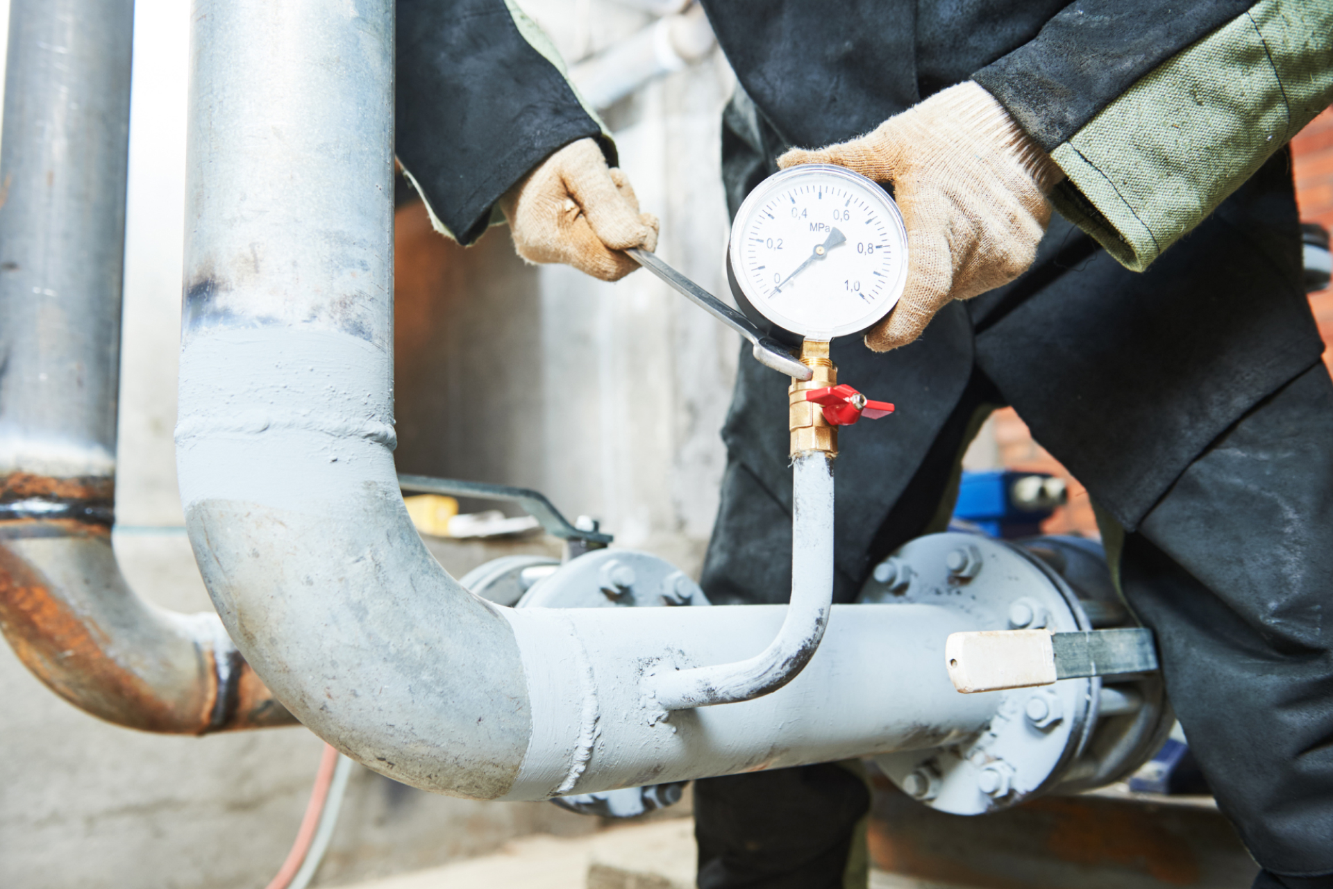 a plumber working to adjust the pressure regulator valve in a basement with a wrench