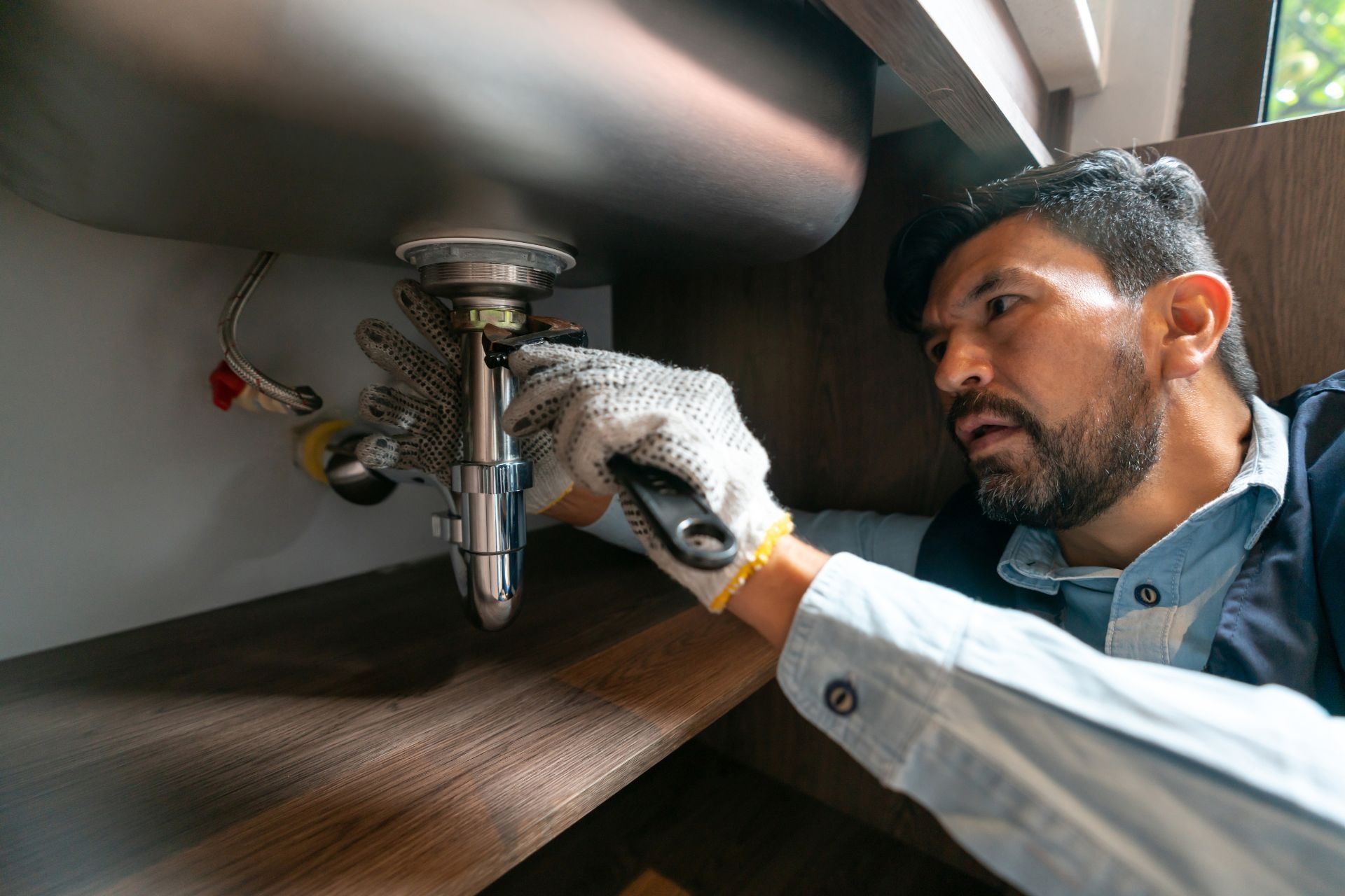 A plumber locking the drain pipe nut underneath a kitchen sink 