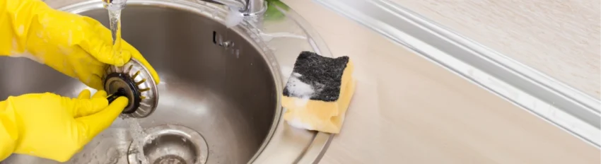 A person cleans a smelly kitchen sink drain with dish soap and hot water