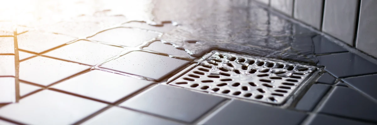 A close-up of water flowing toward a square stainless steel point drain set in dark grey shower floor tiles