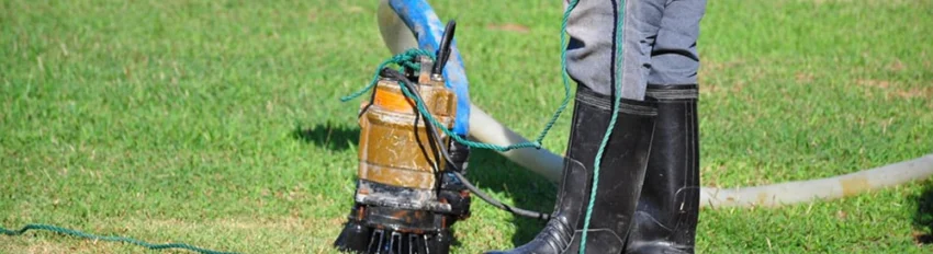 Man in boots cleaning a sump pump in the yard
