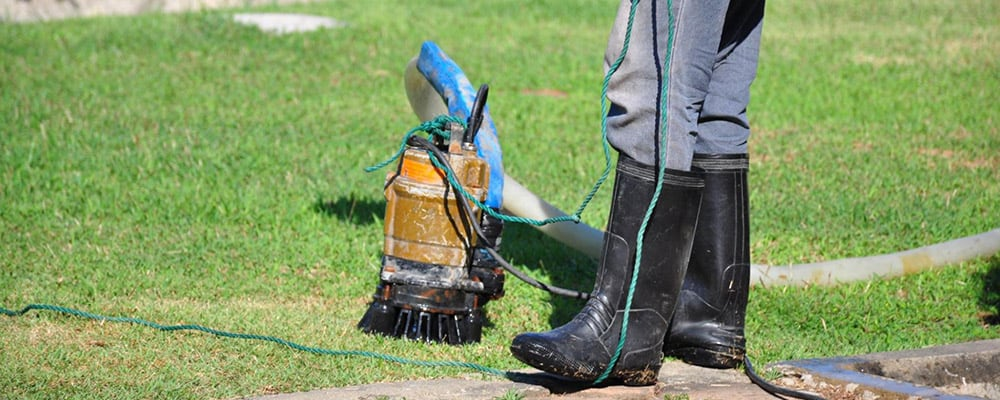 Man in boots cleaning a sump pump in the yard